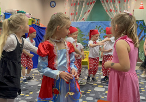 Z przodu trzy dziewczynki. W środku, w roli Śnieżki dziewczynka w niebiesko-czerwonej sukience. Za nimi chłopcy w strojach krasnoludków. Z lewej strony wchodzi macocha w ciemnej sukience.